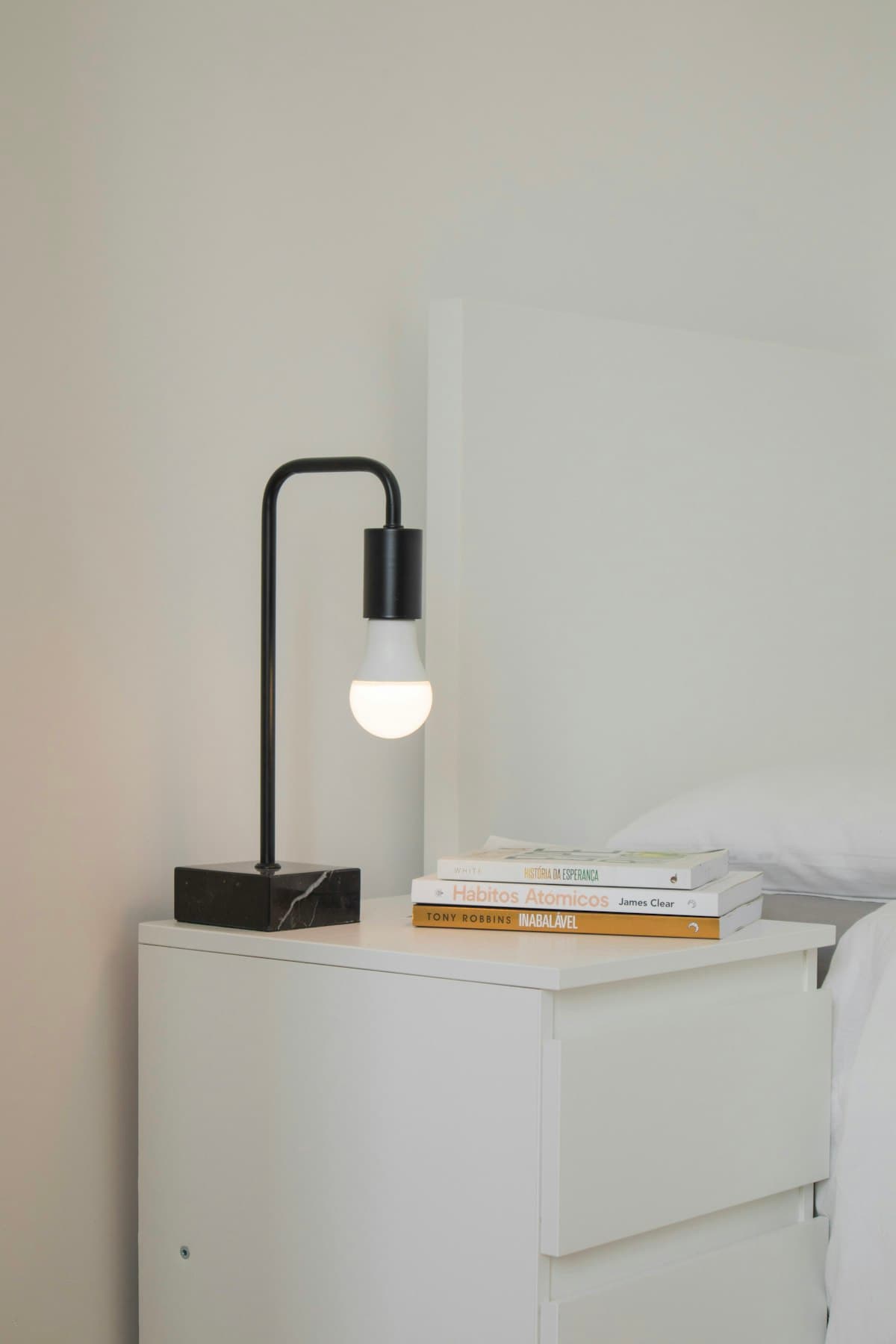 Minimal black desk lamp with a softly glowing bulb on a pale interior surface.